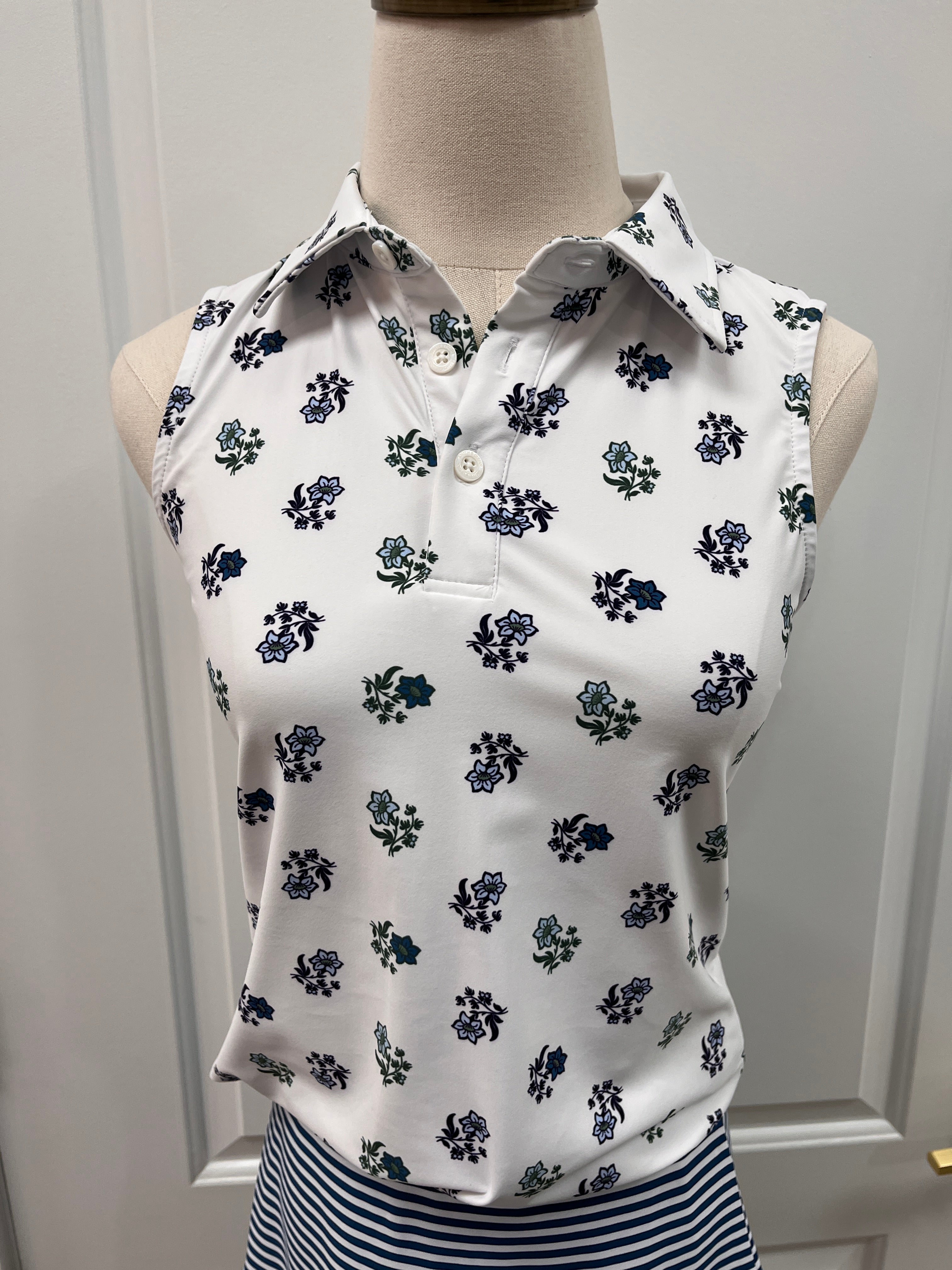 White sleeveless collared top with a navy and green floral print, displayed on a beige dress form mannequin against a white paneled door background.