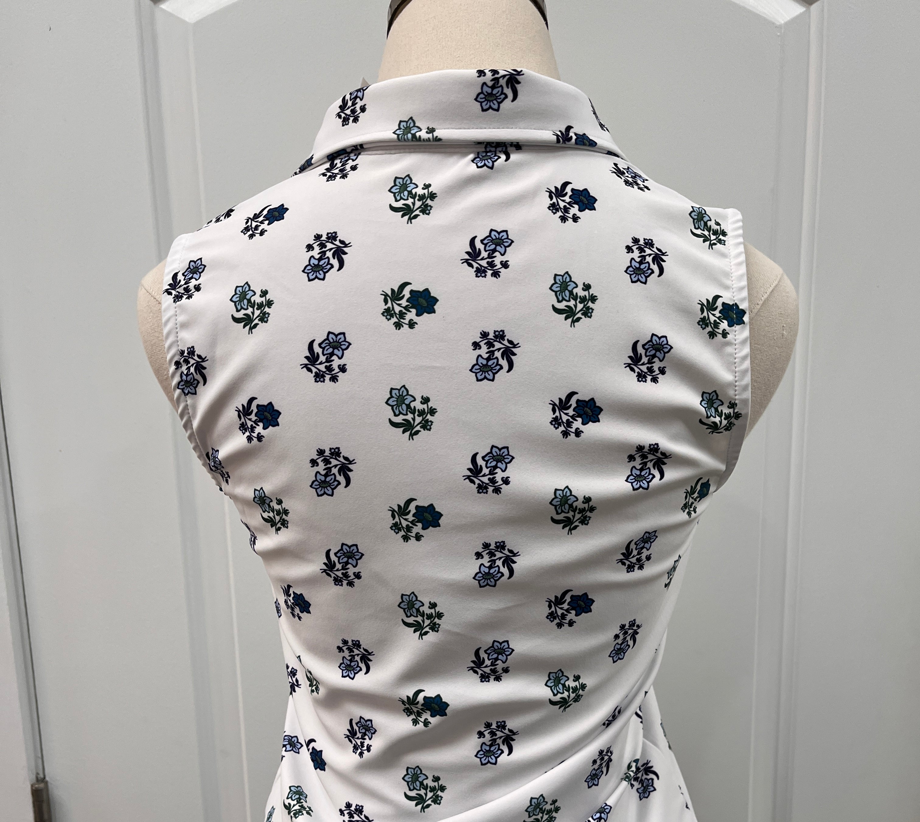A white sleeveless top with a navy blue floral pattern, displayed on a mannequin torso next to a navy and white striped garment, set against a white paneled door background.