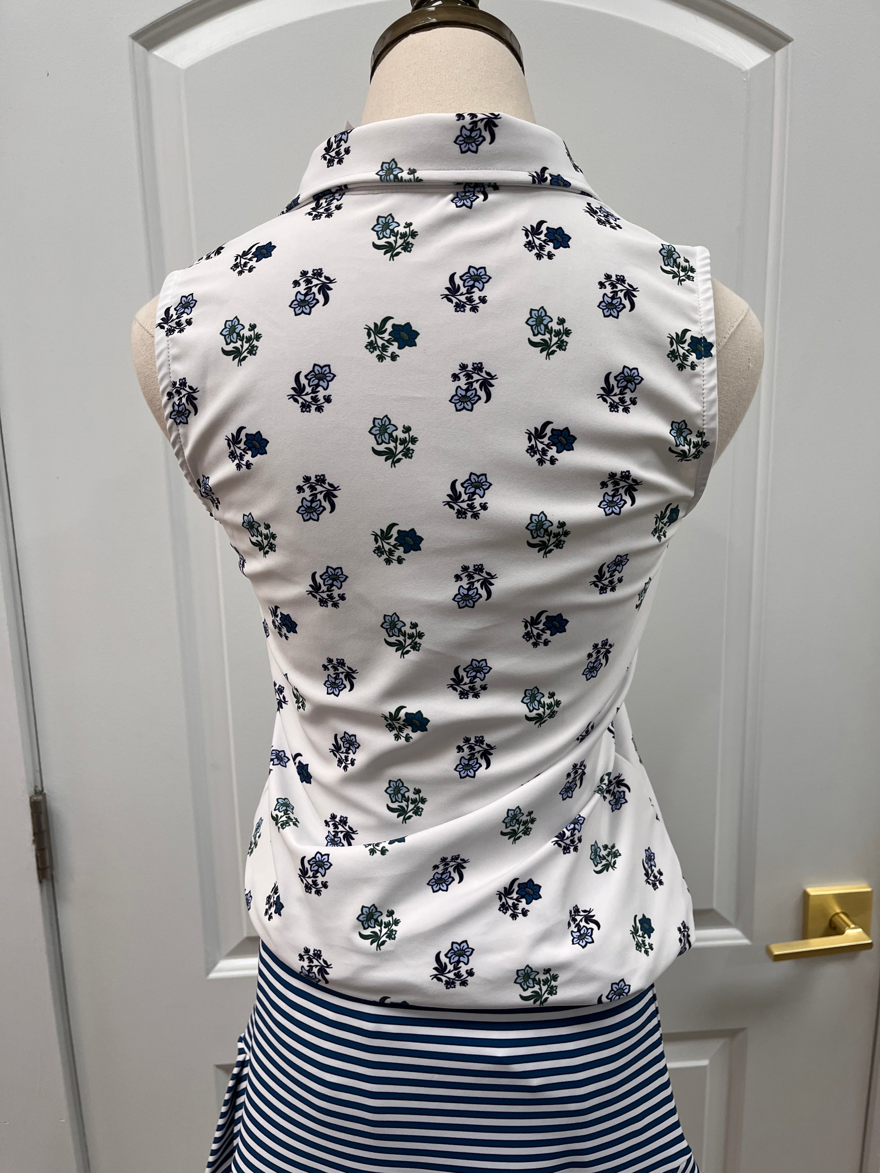 A white sleeveless top with a navy blue floral pattern, displayed on a mannequin torso next to a navy and white striped garment, set against a white paneled door background.