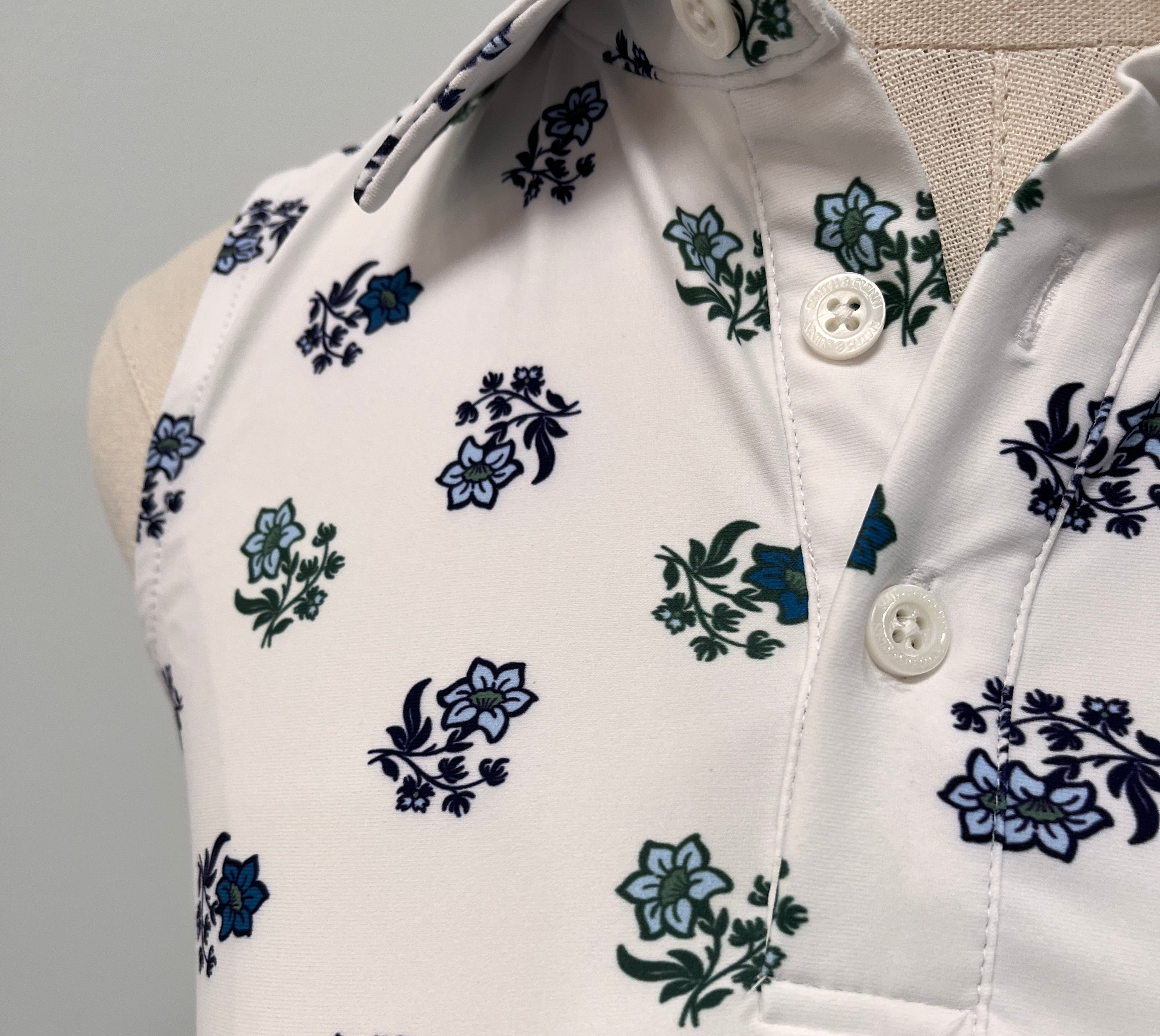 Close-up of a white top with a repeating floral print in blue and green, featuring a buttoned neckline.