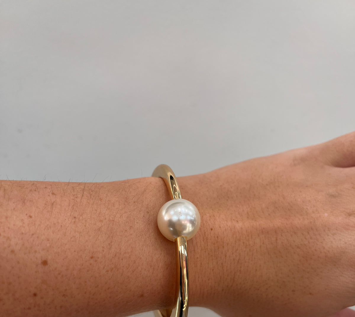 gold hinged cuff bracelet with a single white freshwater pearl,