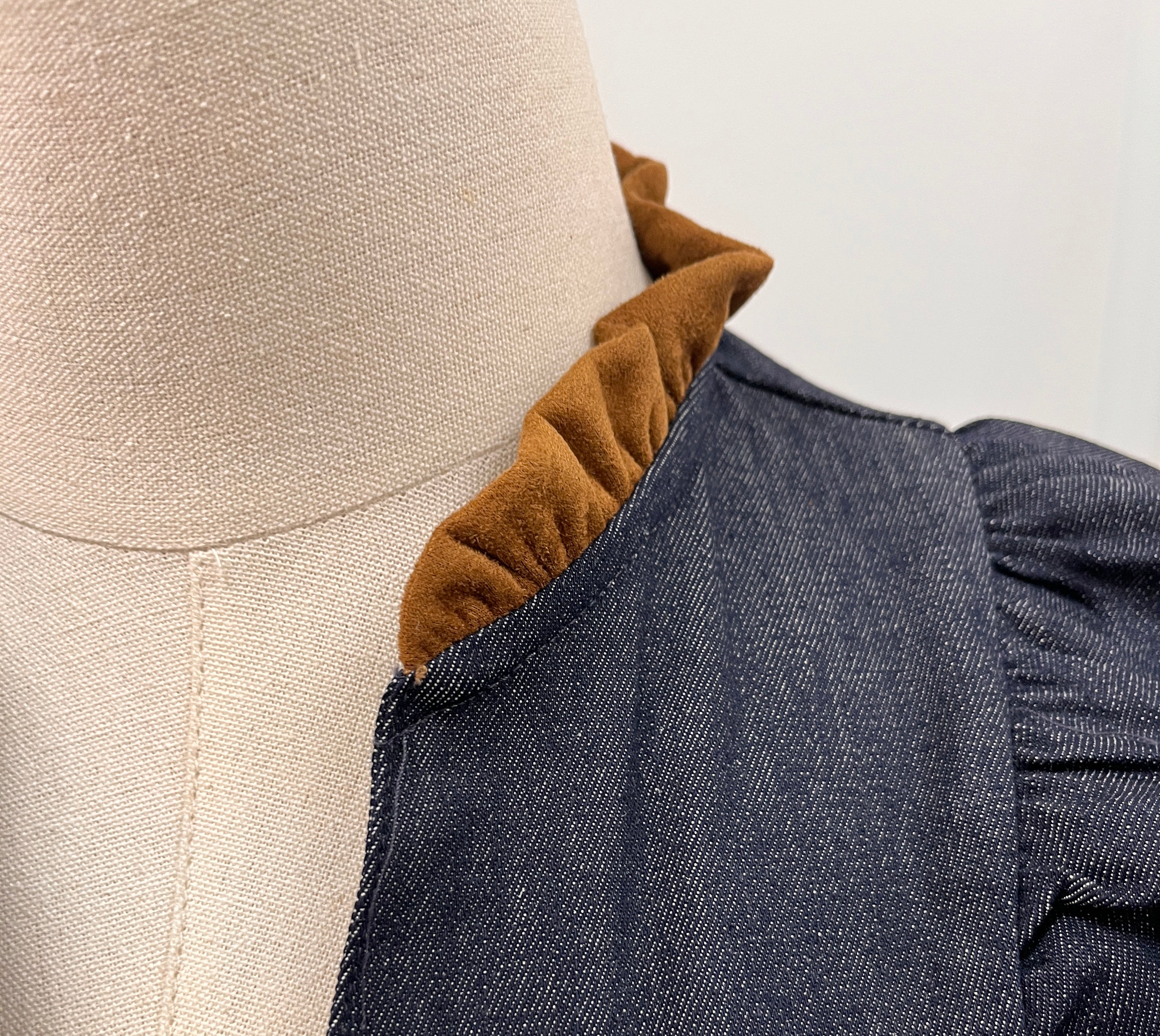 Close-up of a dark blue-gray textured fabric garment with a ruffled mustard-brown inner collar style#JH2528