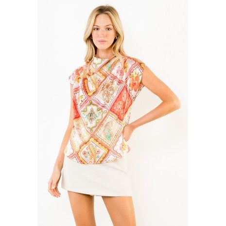 A woman modeling a sleeveless, high-neck top with a colorful patchwork paisley print in shades of orange, pink, green, and beige, paired with a white mini skirt against a plain white background.