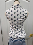A white sleeveless top with a navy blue floral pattern, displayed on a mannequin torso next to a navy and white striped garment, set against a white paneled door background.
