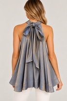 Ainsley Top by Fate in metallic silver-gray with a large tie-back bow, trailing ties, and flared hem, back view.