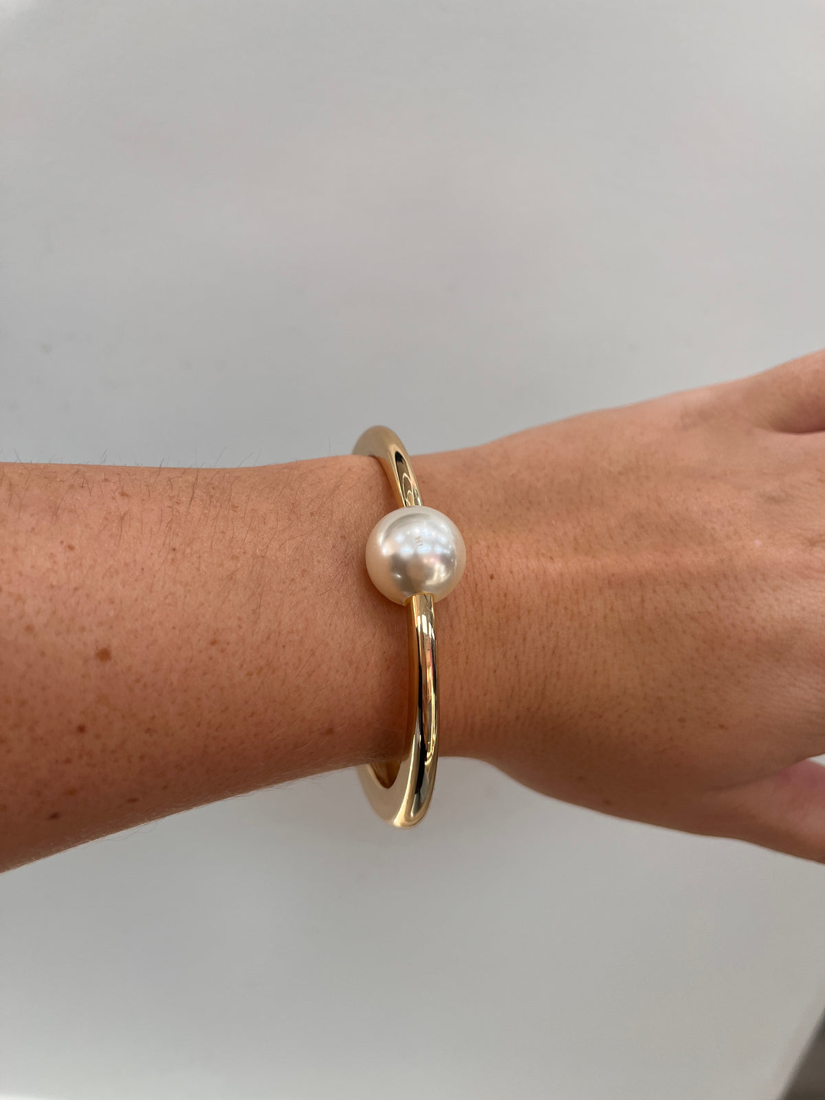 gold hinged cuff bracelet with a single white freshwater pearl,