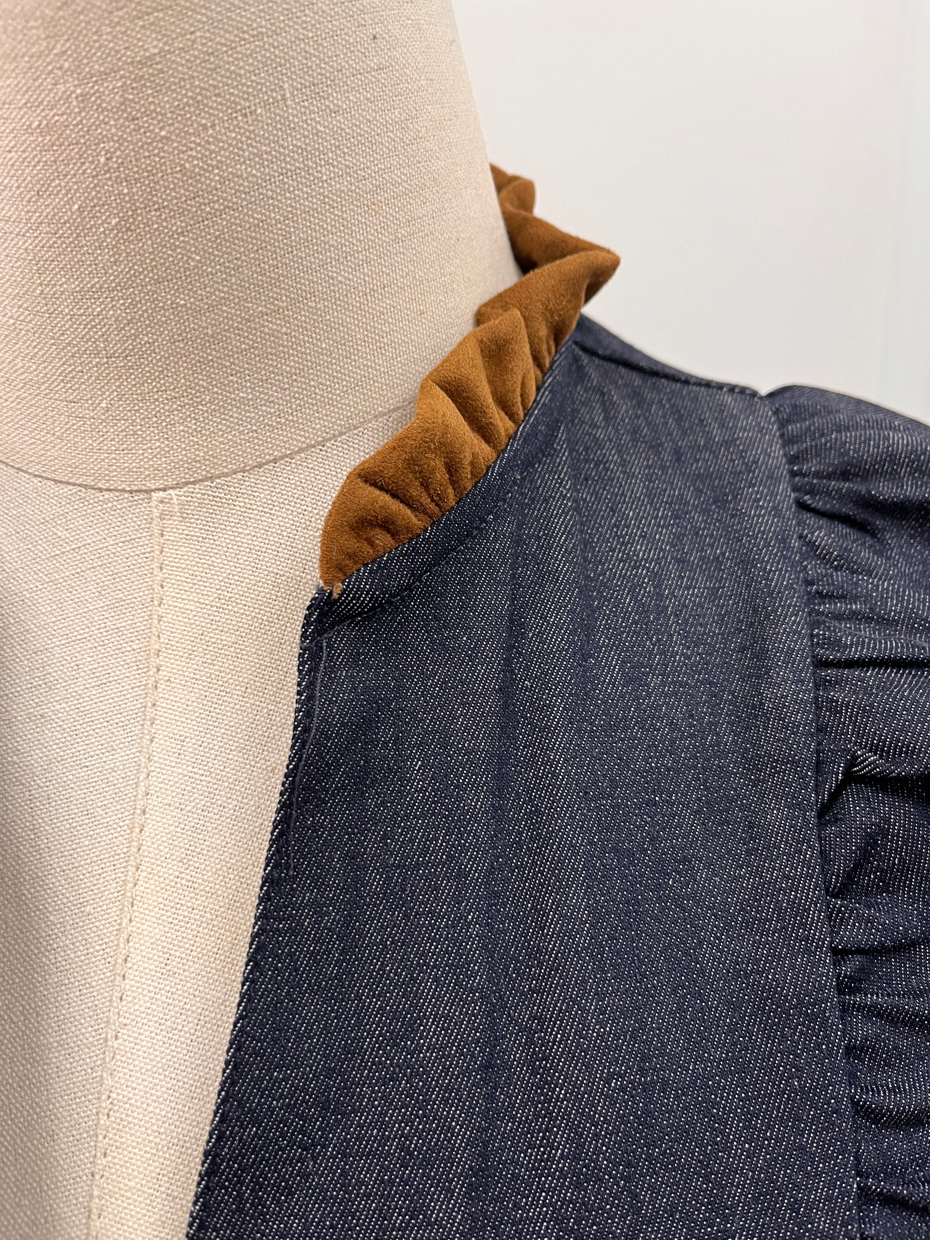 Close-up of a dark blue-gray textured fabric garment with a ruffled mustard-brown inner collar style#JH2528