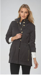 Woman wearing a dark gray parka with gold buttons on a light gray background