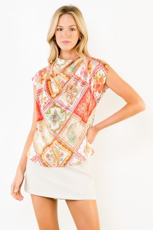 A woman modeling a sleeveless, high-neck top with a colorful patchwork paisley print in shades of orange, pink, green, and beige, paired with a white mini skirt against a plain white background.